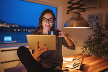 Dedicated Female Student Utilizing Tablet and Laptop to Prepare for Real Estate Exam with Night City Background while in her home - NightBeforeTheExam.com for Comprehensive Real Estate Study